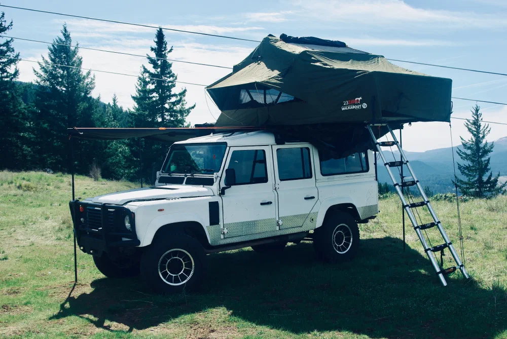Side view of the Perentie 110 with rooftop tent deployed and ladder down at a grassy campsite