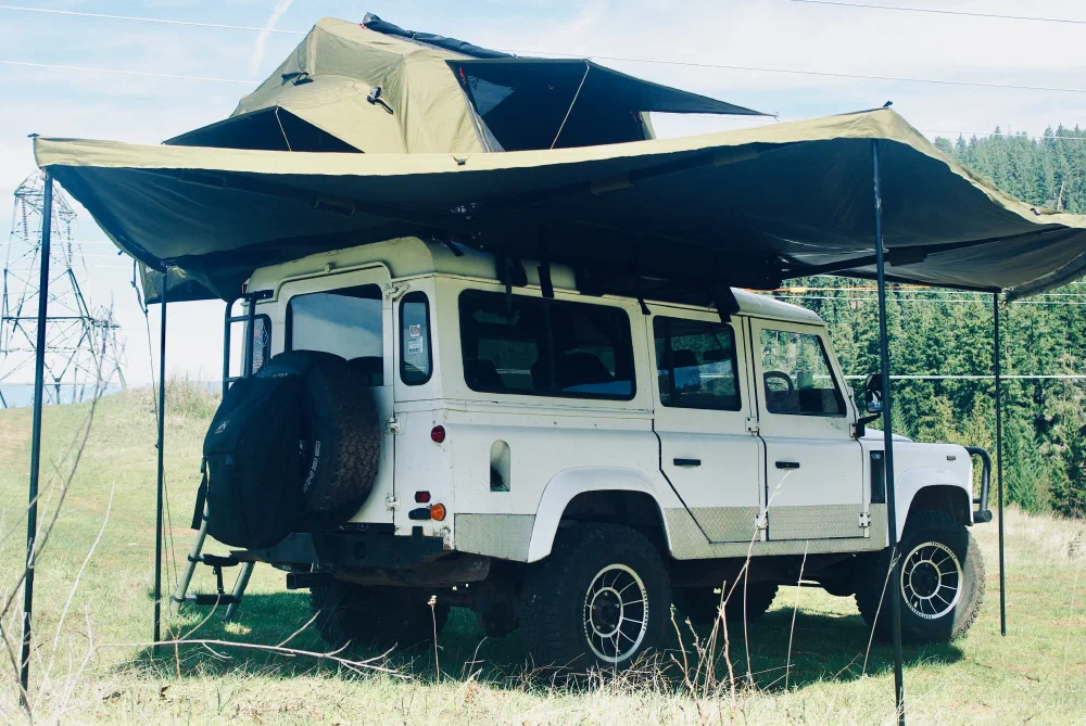 Rear three-quarter view of the Perentie 110 with rooftop tent deployed in a mountain meadow