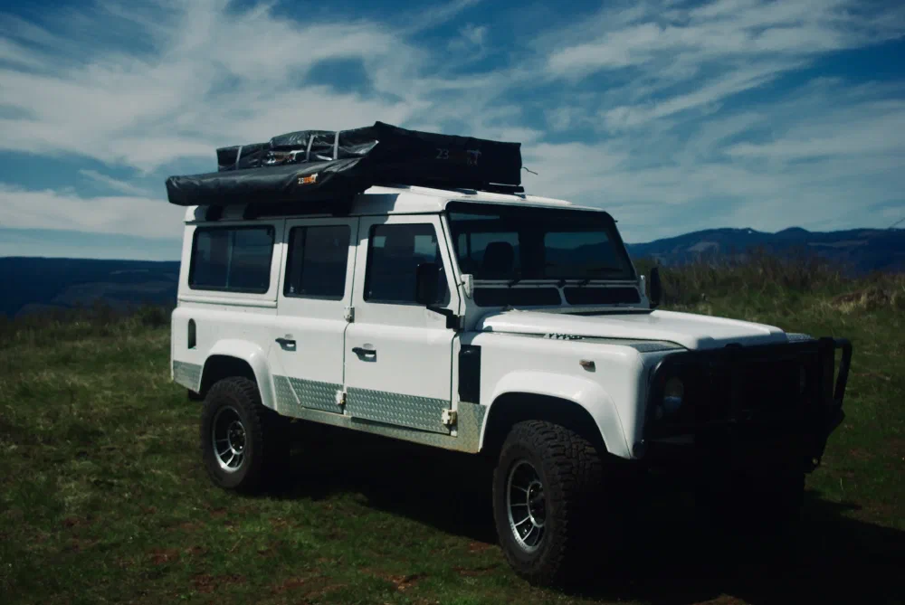 Side view of the Perentie 110 with rooftop tent and awning on a hillside with power lines