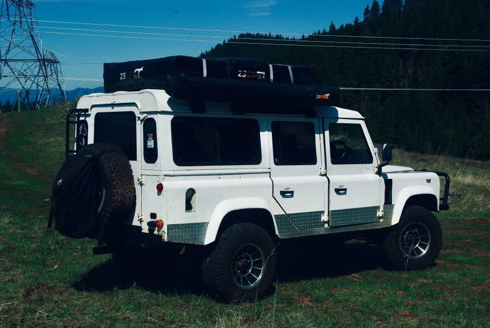 Three-quarter rear view of the Perentie 110 with rooftop tent and awning in a grassy field