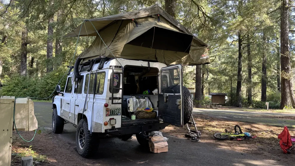 Perentie 110 at a forest campsite with rooftop tent deployed
